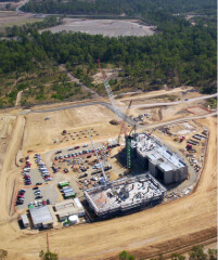 Aerial view of the construction of UniSQ Springfield, with cranes, vehicles, and a partially built industrial building surrounded by trees and dirt areas.