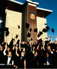 A group of graduates in caps and gowns toss their caps in the air in front of a building at UniSQ Springfield.