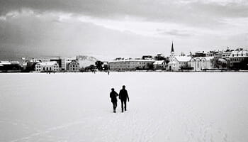 Two people walking in the snow, they are in the distance walking towards a town.