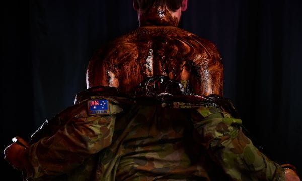 A man in an army uniform with molasses on his back facing away from the camera.