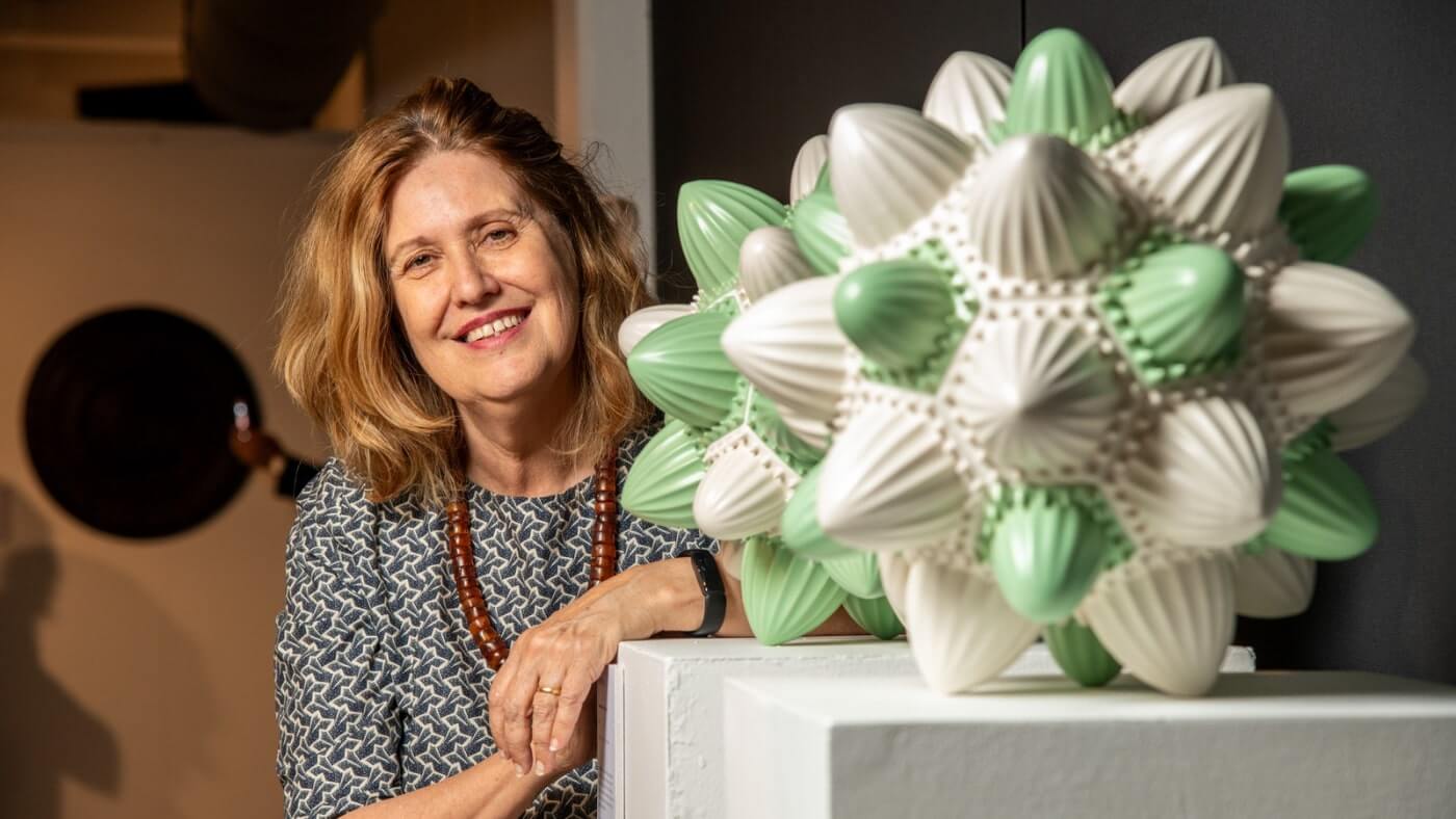 Person smiling next to a geometric sculpture with green and white spiked elements on display.