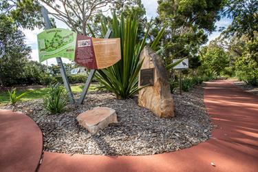 Gumbi Gumbi Gardens with informational signs, a large rock with a plaque.