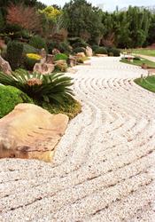 A Zen garden with carefully raked gravel patterns, large stones, and lush green shrubs at UniSQ Japanese Garden.