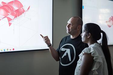 A man in a black t-shirt pointing at a 3D mathematical graph on a screen, with a woman standing next to him.