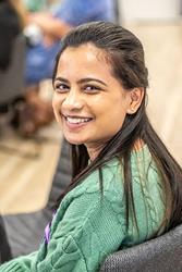 A woman with a green sweater and long dark hair smiles while seated. She is looking slightly to her left.