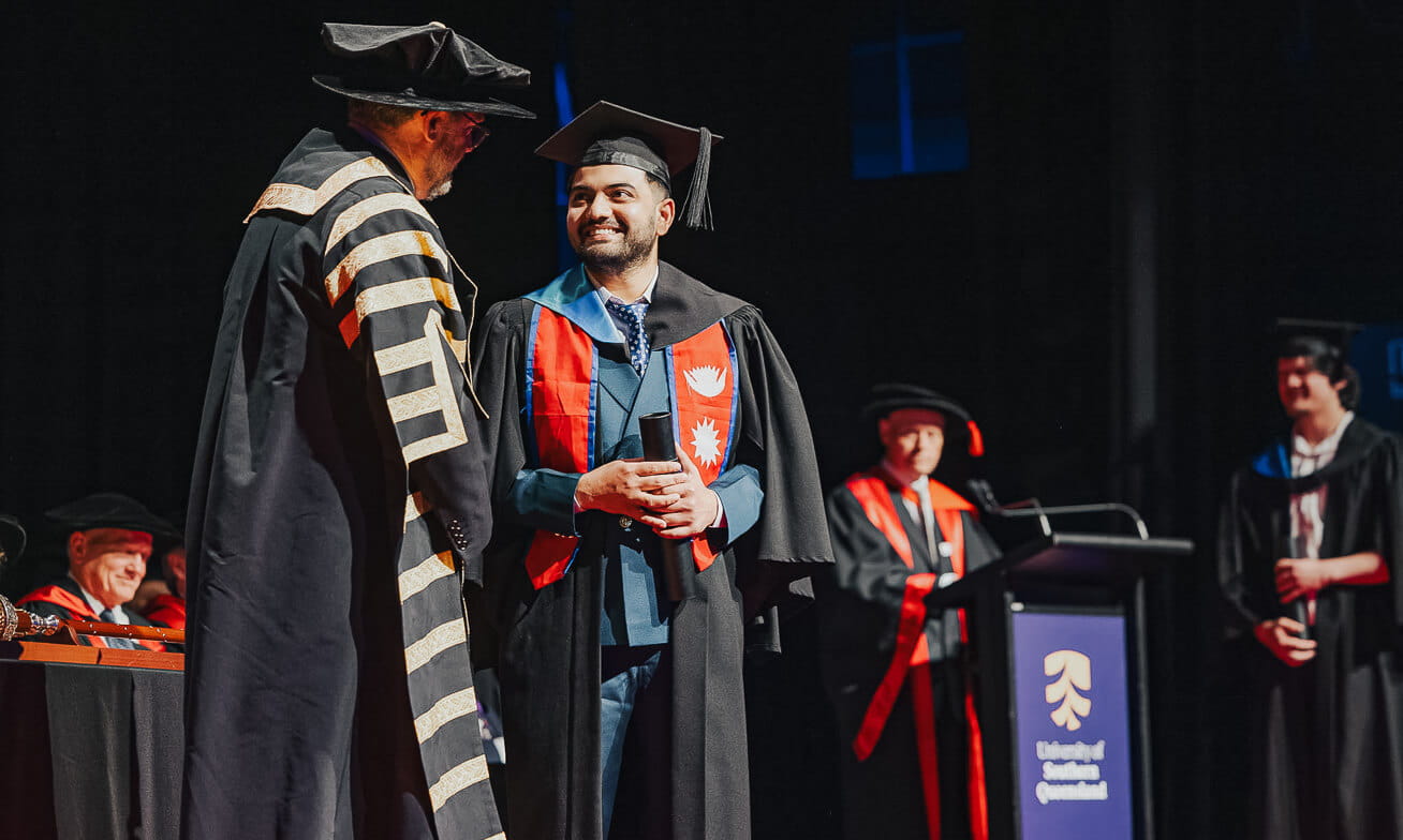 A graduate in cap and gown shakes hands with a university official during a graduation ceremony on stage.