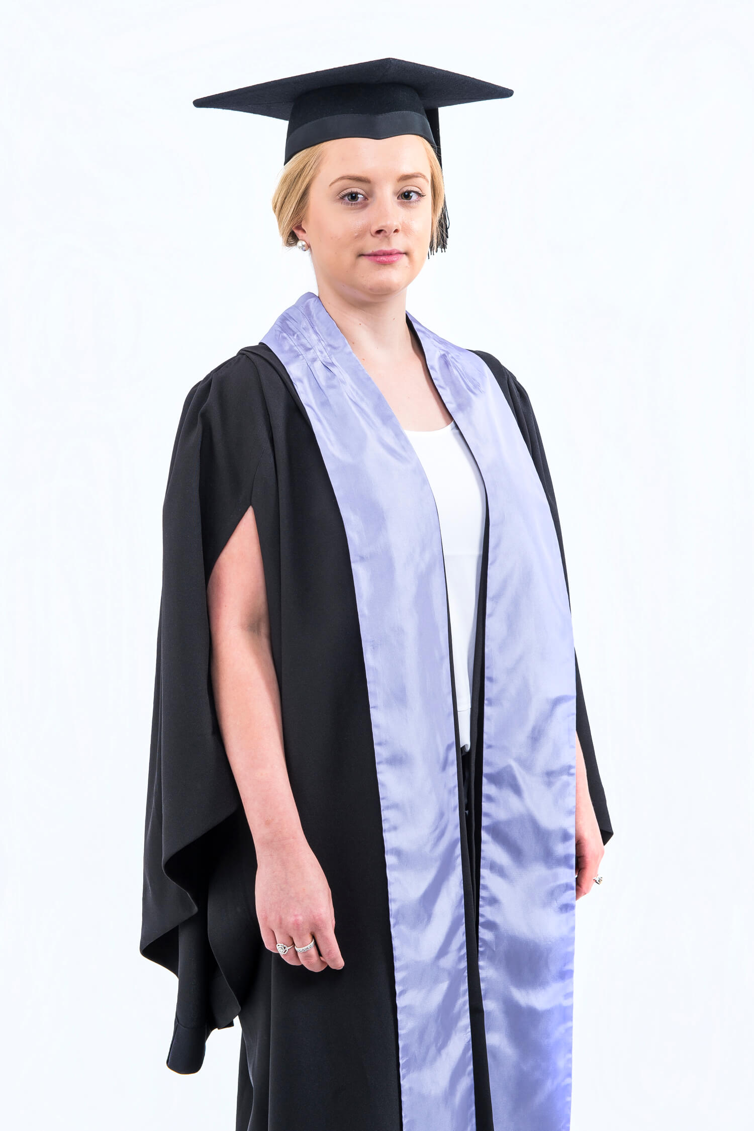 A graduate wearing a black cap and gown with a purple stole stands against a white background.