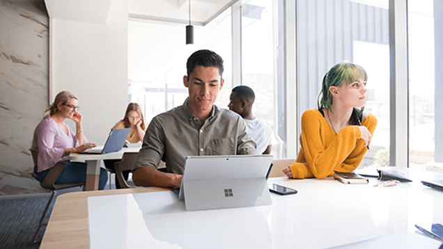 Five people work and converse in a modern office space, with laptops and smartphones on the tables.