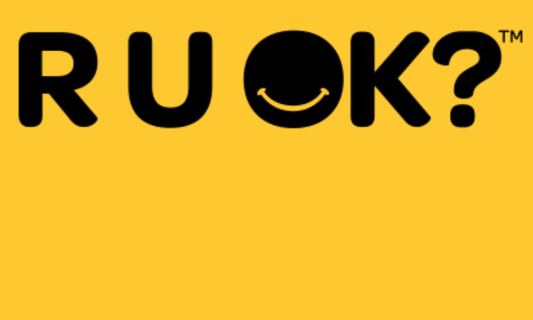 Yellow background with the text “R U OK?” in black, where the letter “O” is a black circle featuring a small yellow smiling mouth.