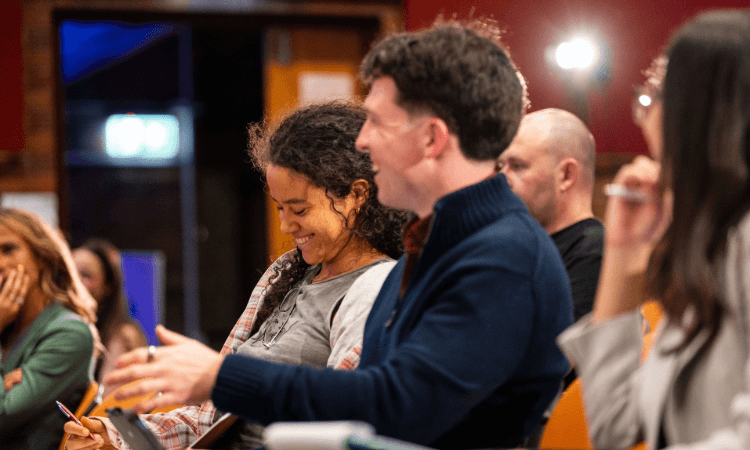 A diverse group of people sitting in a row during a meeting or presentation, with some participants smiling.