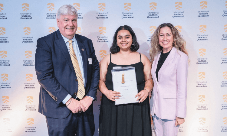 A man in a suit, a young woman holding an award, and a woman in a light-colored blazer standing in front of a University of Southern Queensland step-and-repeat backdrop.