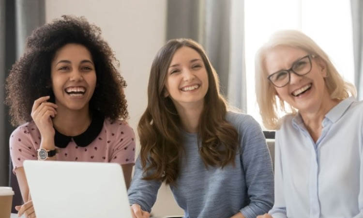 Three women of different ages smiling and looking at a laptop together.