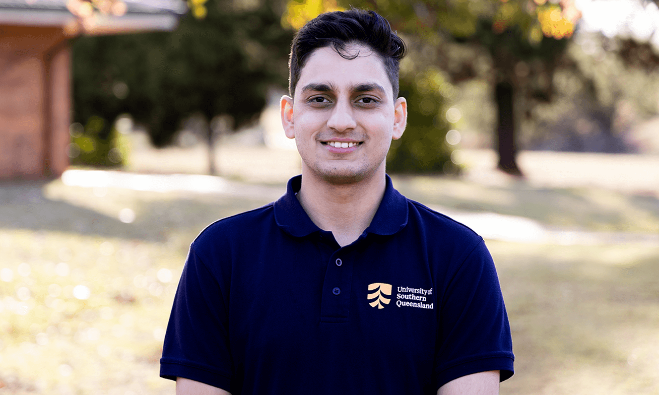 A person wearing a University of Southern Queensland polo shirt stands outdoors, smiling at the camera with trees and grass in the background.