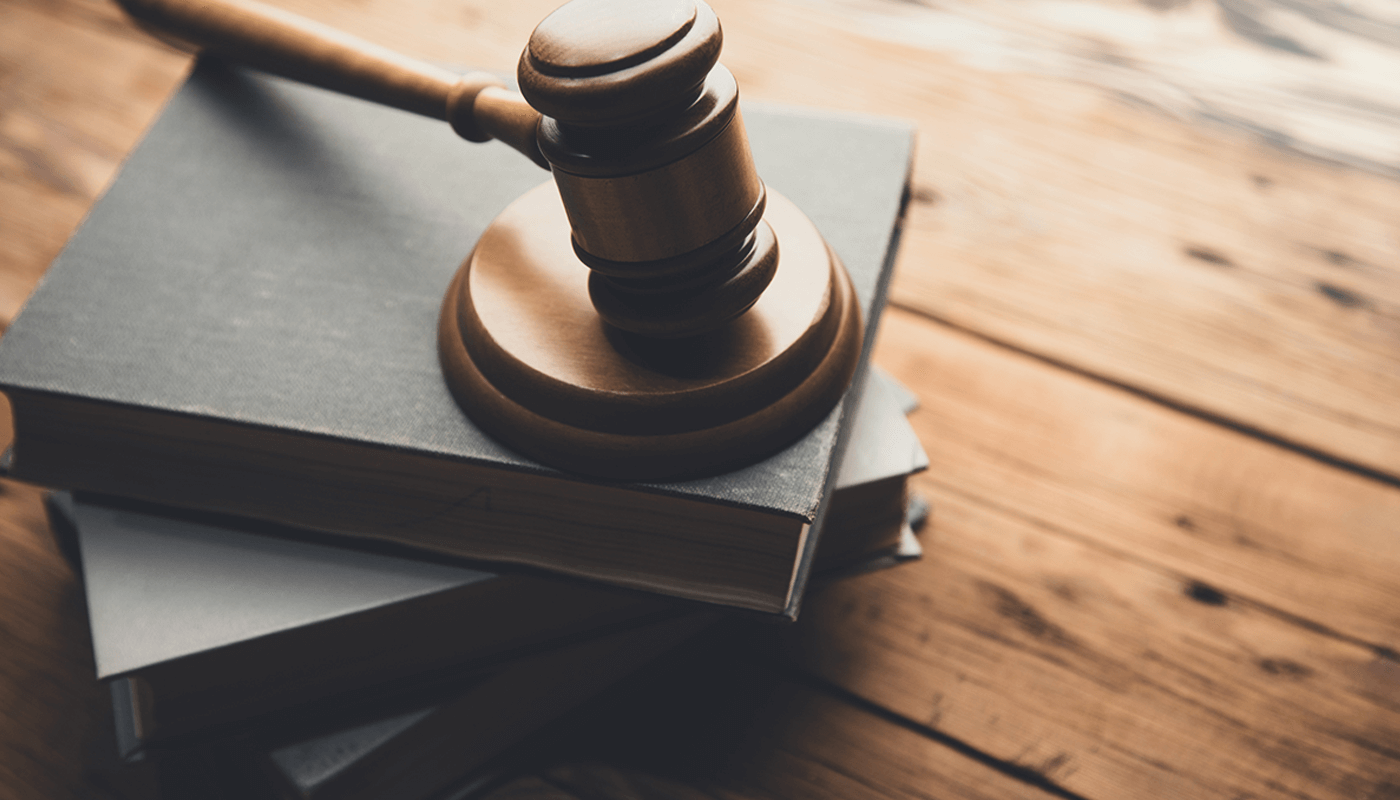 A wooden judge's gavel rests on top of a stack of books on a wooden table.