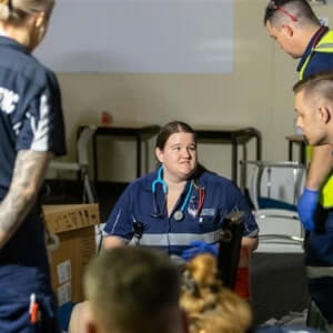 A medical professional with a stethoscope around her neck sits and talks to three standing colleagues in a clinical setting.