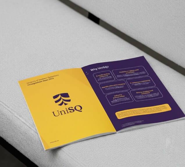 An open UniSQ booklet rests on a light gray couch, displaying the University of Southern Queensland logo and informational content about the university.