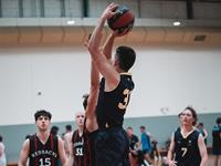 A basketball player in a UniSQ jersey prepares to shoot while being closely defended; other players and spectators are visible in the background.