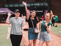 Three young people stand outside, smiling and waving at the camera. 