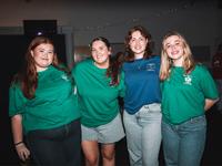 Four young people stand together indoors, all smiling at the camera.