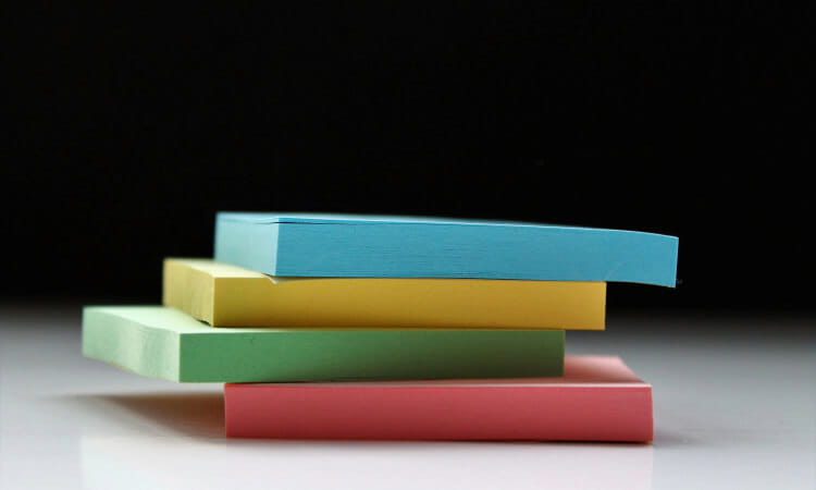 A stack of four sticky note pads in blue, yellow, green, and red against a black background.
