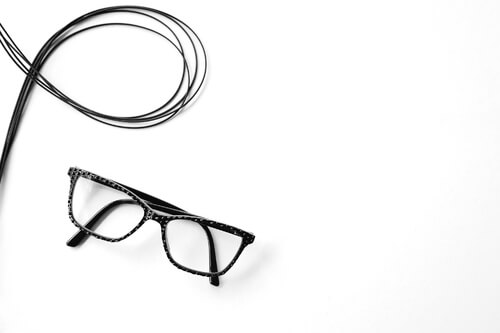 Eye glasses placed near a coiled black cable on white background