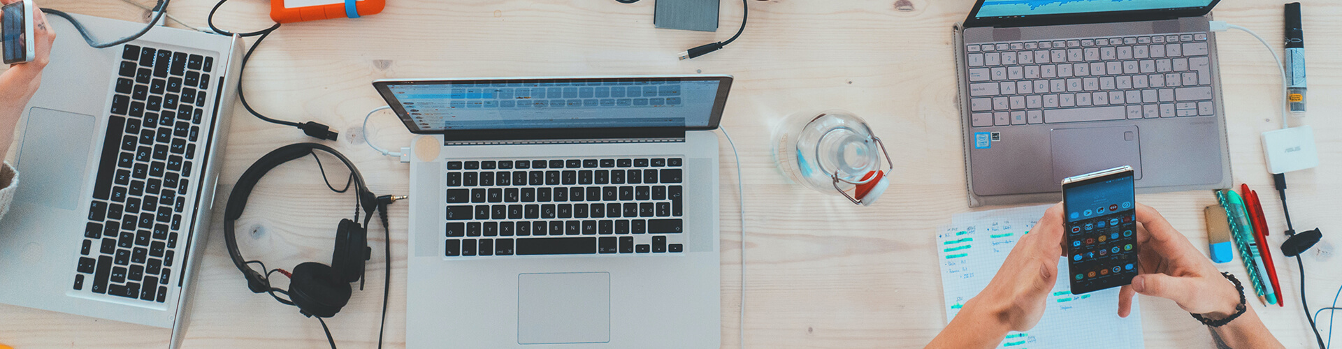 Two people working at a desk with laptops, smartphones, and various office supplies.