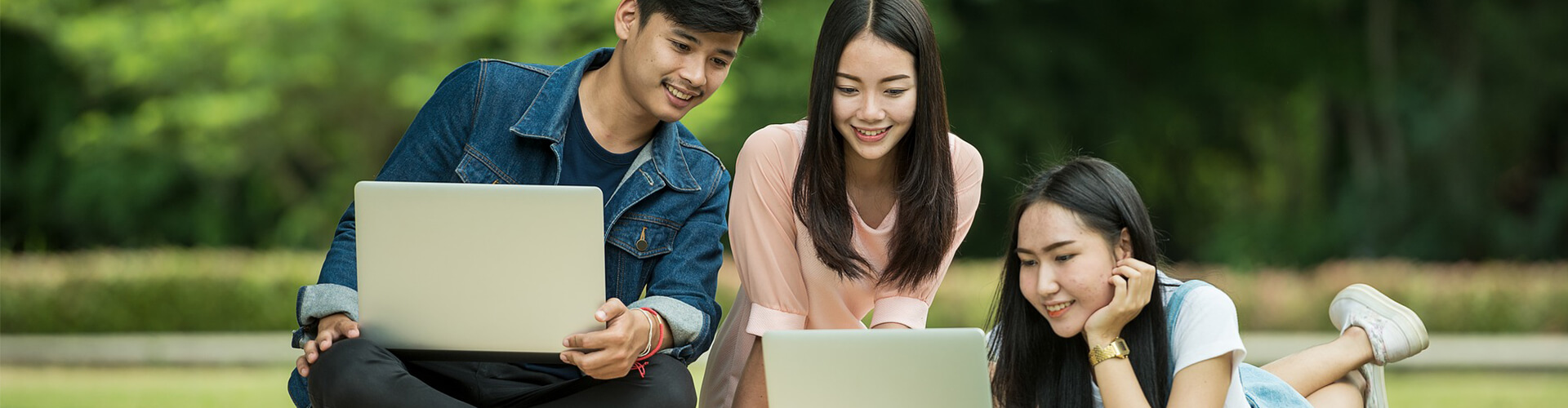 Three students sitting outside with laptops