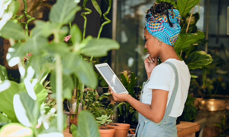 Lady looking at an iPad while standing in front of plants.