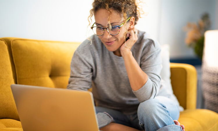 Lady working on a laptop sitting on a couch.