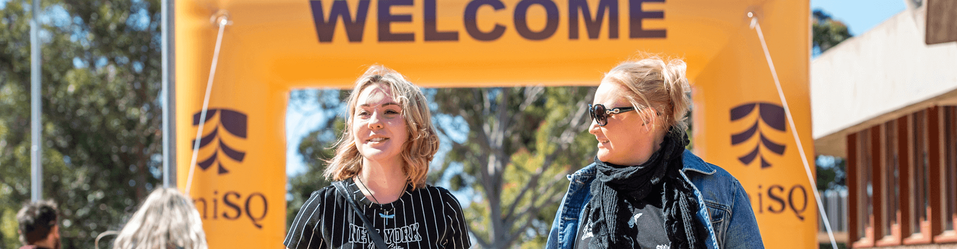 Smiling people in front of UniSQ inflatable welcome arch.