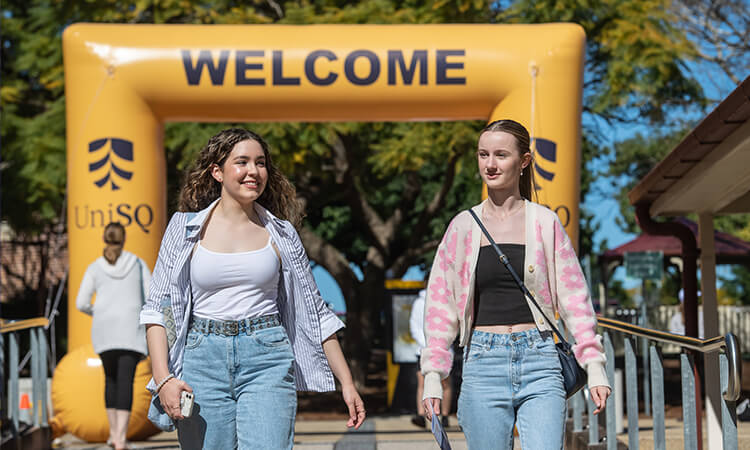 Two women walking under a UniSQ Welcome arch.