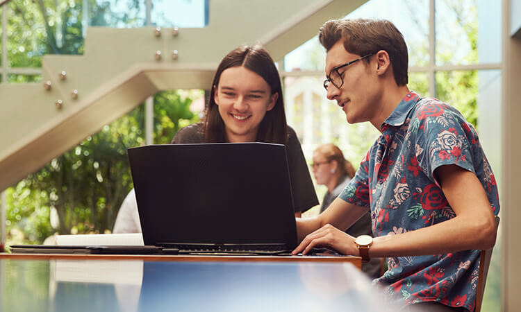 Two male students sitting at a laptop in the UniSQ Ipswich Library.