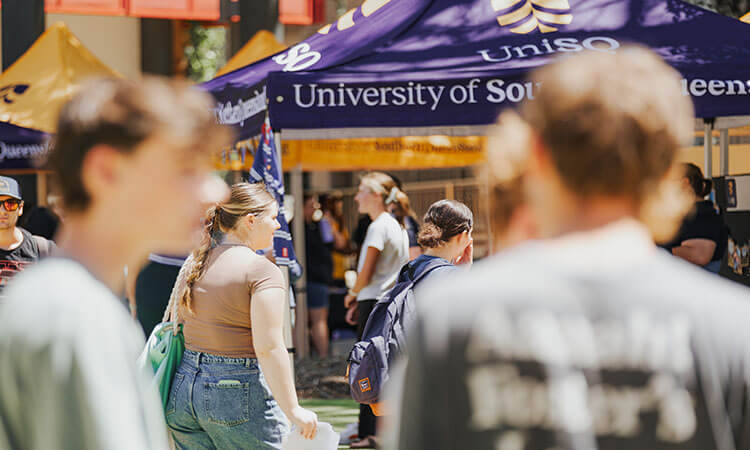 Students walk around outdoor university stalls, including one with a prominent University of Southern Queensland (UniSQ) tent in the background.