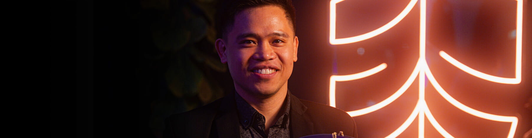 A person smiling in front of a neon-lit background.