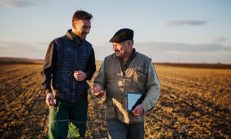 Young man talks to old man in field.