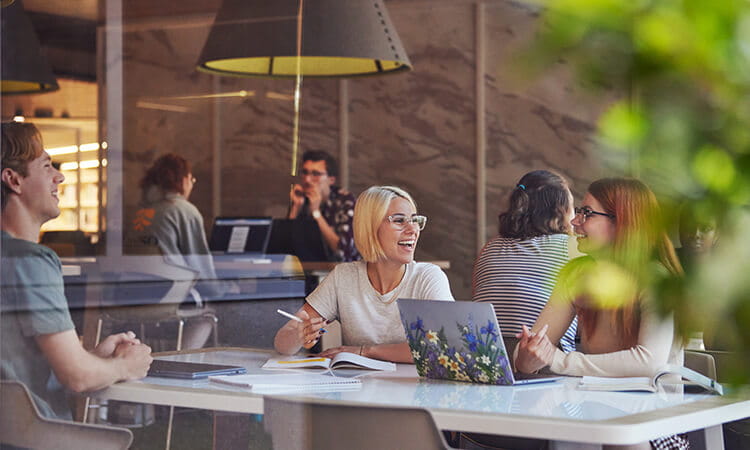 Three students sitting at a table and talking in the UniSQ Springfield Library.