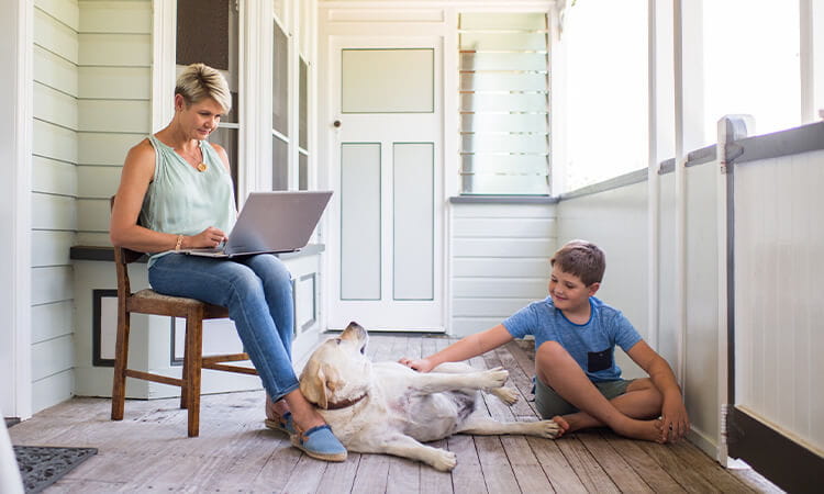 A lady working on her laptop with her son and dog near her.