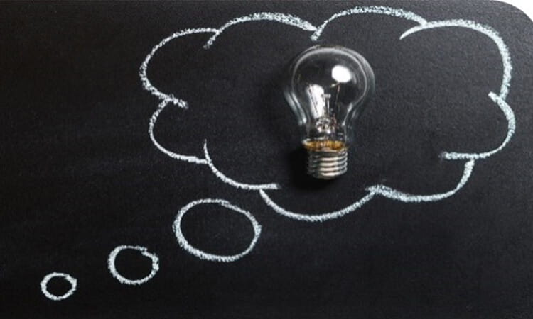 A light bulb placed on a dark surface with a chalk-drawn thought bubble around it.