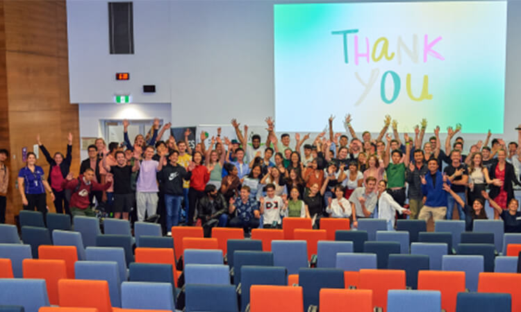Group of people celebrating or expressing appreciation in an auditorium with the words "thank you" projected on the screen behind them.