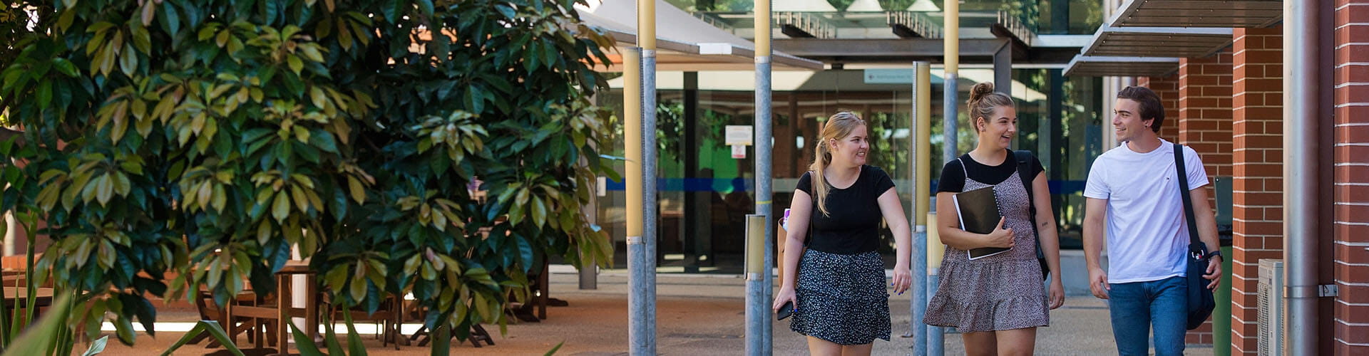 Three students walking side-by-side at a UniSQ campus not looking at camera talking amongst themselves