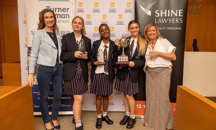 A group of girls holding trophies in front of a banner.