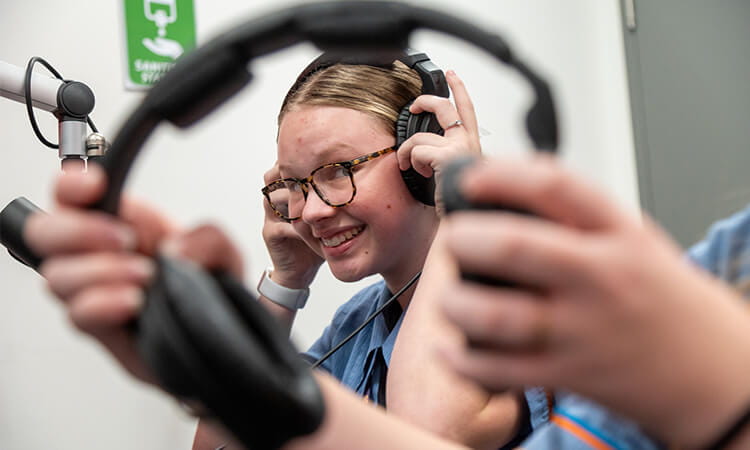 Person smiling while putting on over-ear headphones.