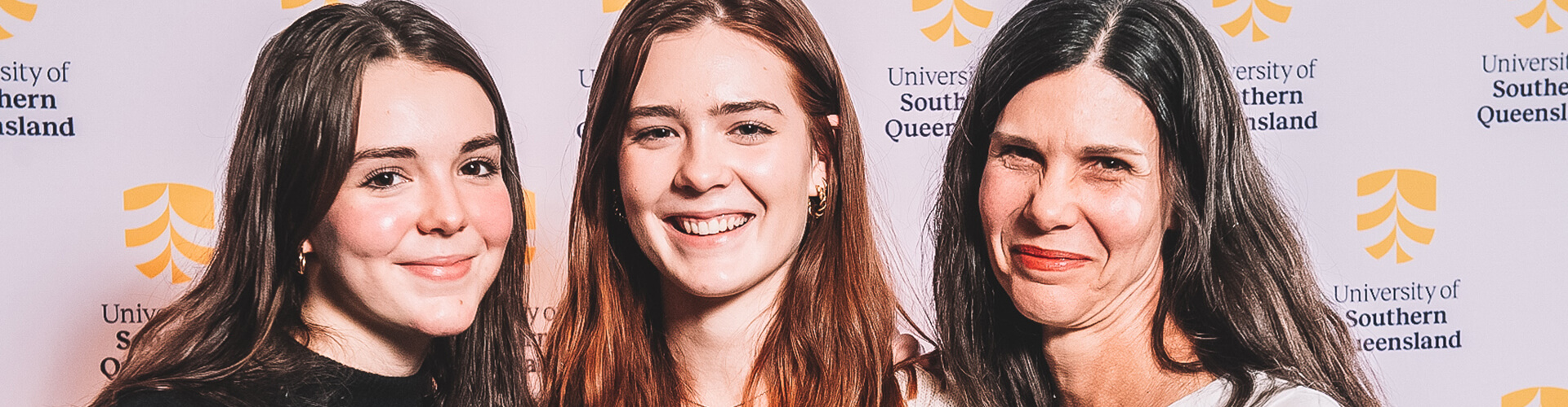Three women posing with smiles at an event by the university of southern queensland.