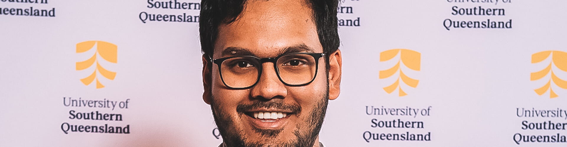 Man with glasses smiling at a university of southern queensland event.