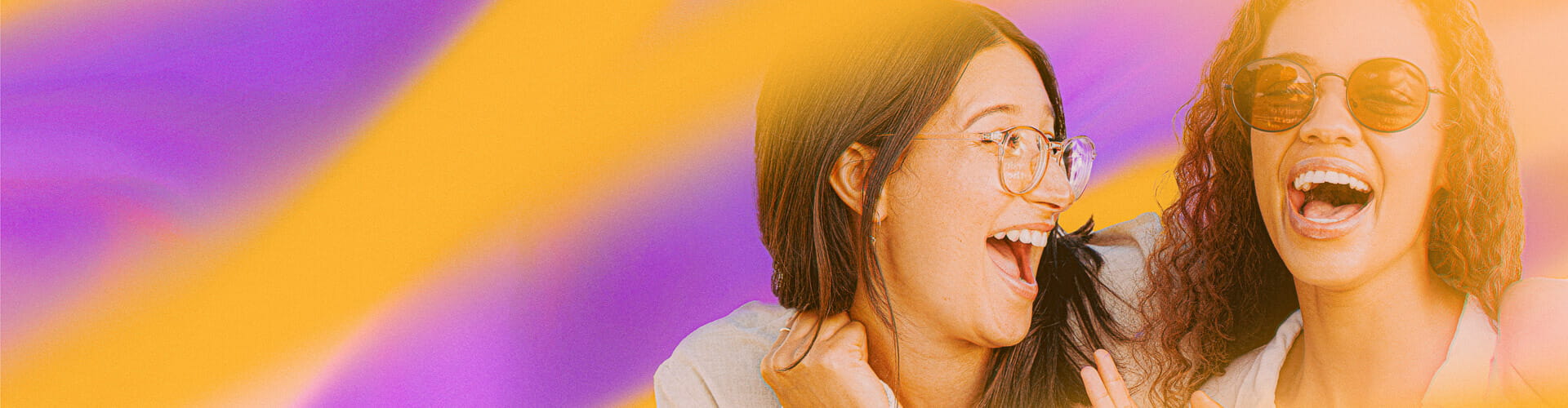 Two women smiling and laughing, one with glasses and the other wearing sunglasses, against a vibrant background with yellow and purple hues.