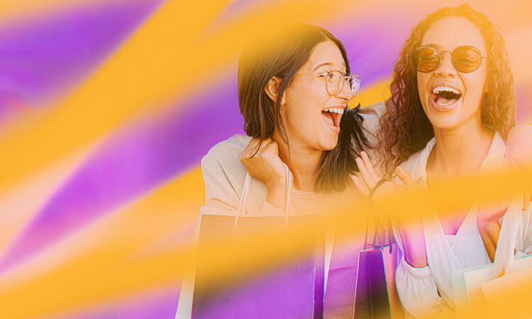 Two young women laughing while holding shopping bags, with a vibrant background featuring orange and purple hues.