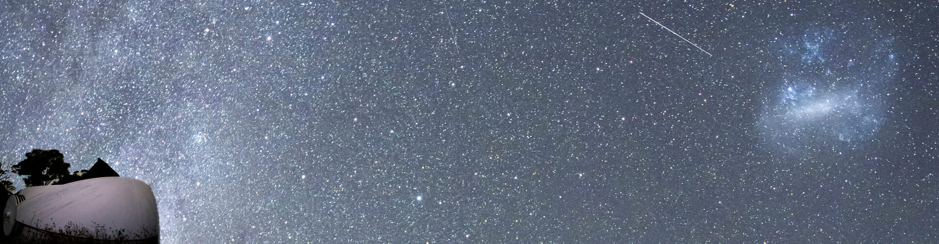 A clear night sky filled with stars and a streak of a meteor. An observatory dome is visible in the left foreground.