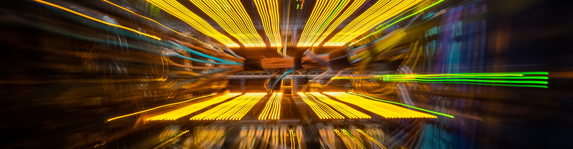 Blurred lights in motion create a dynamic, abstract pattern with streaks of yellow and green on a dark background.
