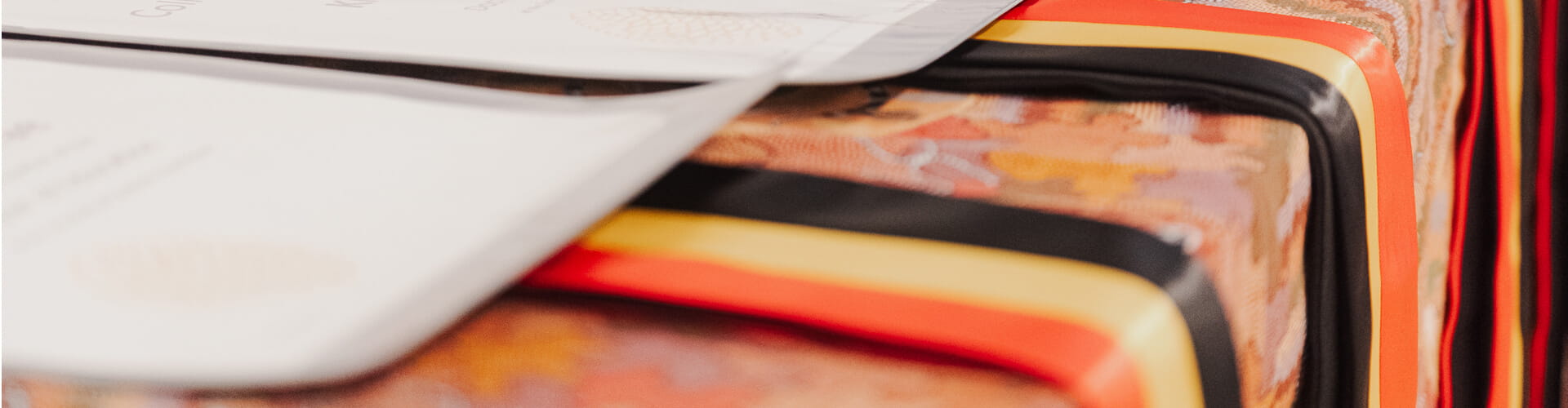 Close-up of neatly folded fabric resembling red, black, and gold ribbons next to a stack of documents.