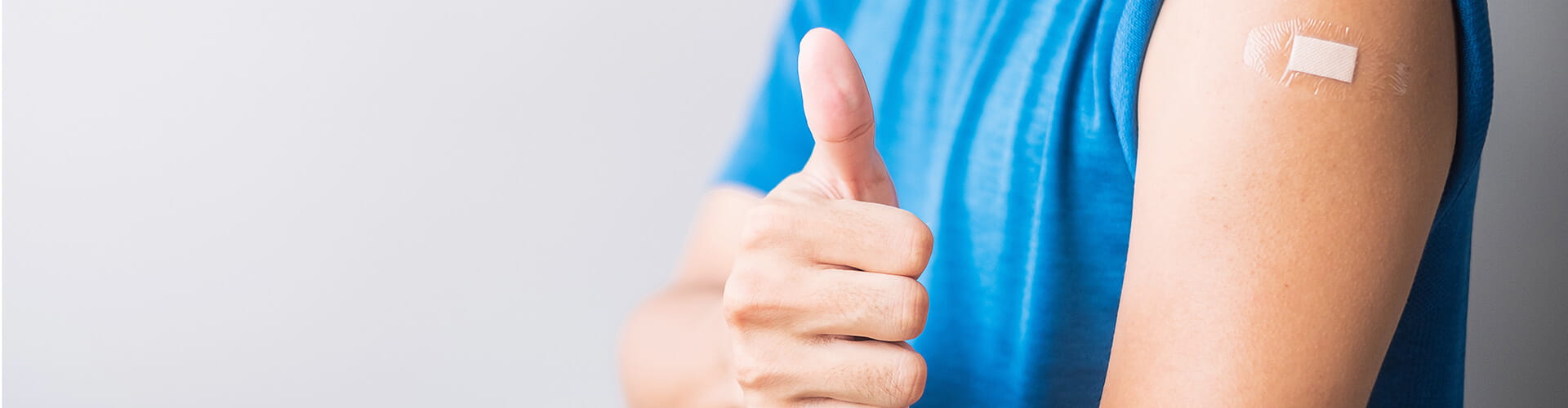 Person in a blue shirt gives a thumbs up, showing an adhesive bandage on their upper arm.
